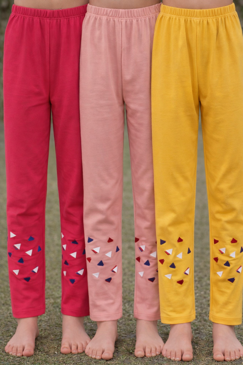 Three pairs of colorful pants with decorative patterns on a grassy background.


